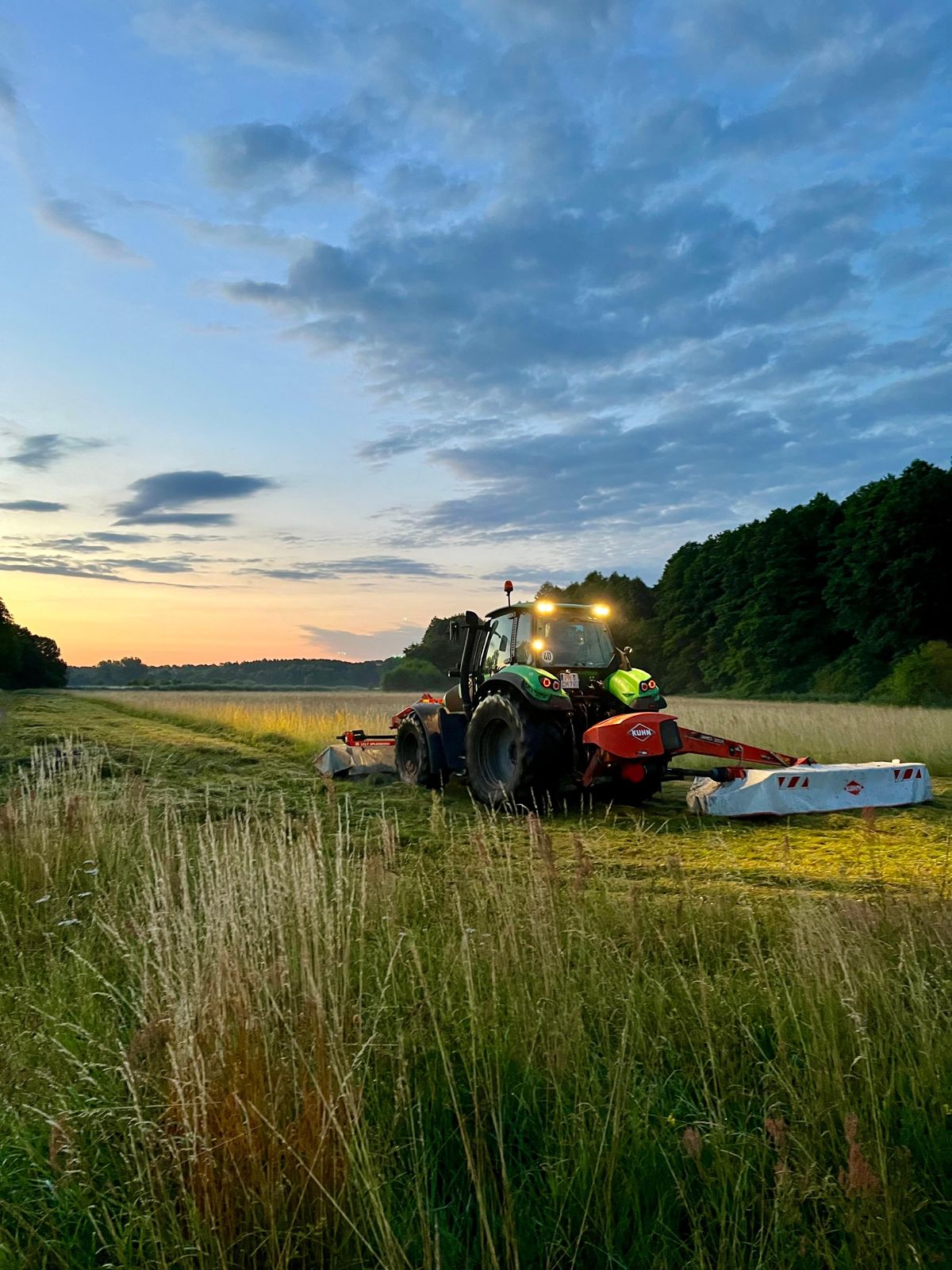 Traktor mit Mähwerk in der Abenddämmerung auf der Wiese